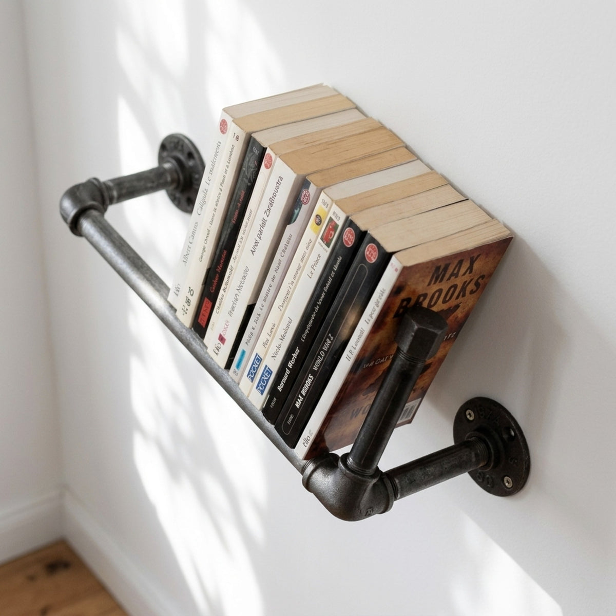 Bibliothèque murale en fonte fixée sur un mur clair avec livres de poche, mise en situation