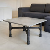 Piètement de table basse en croix, fonte et acier vernis Ø 42 mm, en situation sous un plateau en béton clair poli