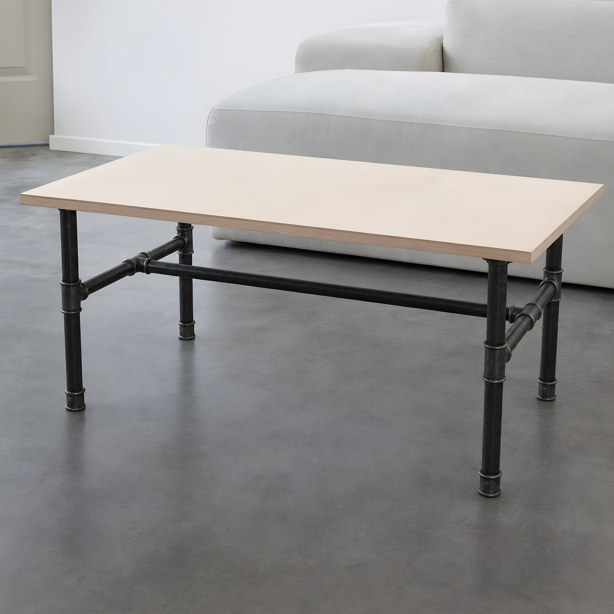Piètement de table basse en H, fonte et acier noir verni Ø 27 mm, en situation sous un plateau en contreplaqué de bouleau